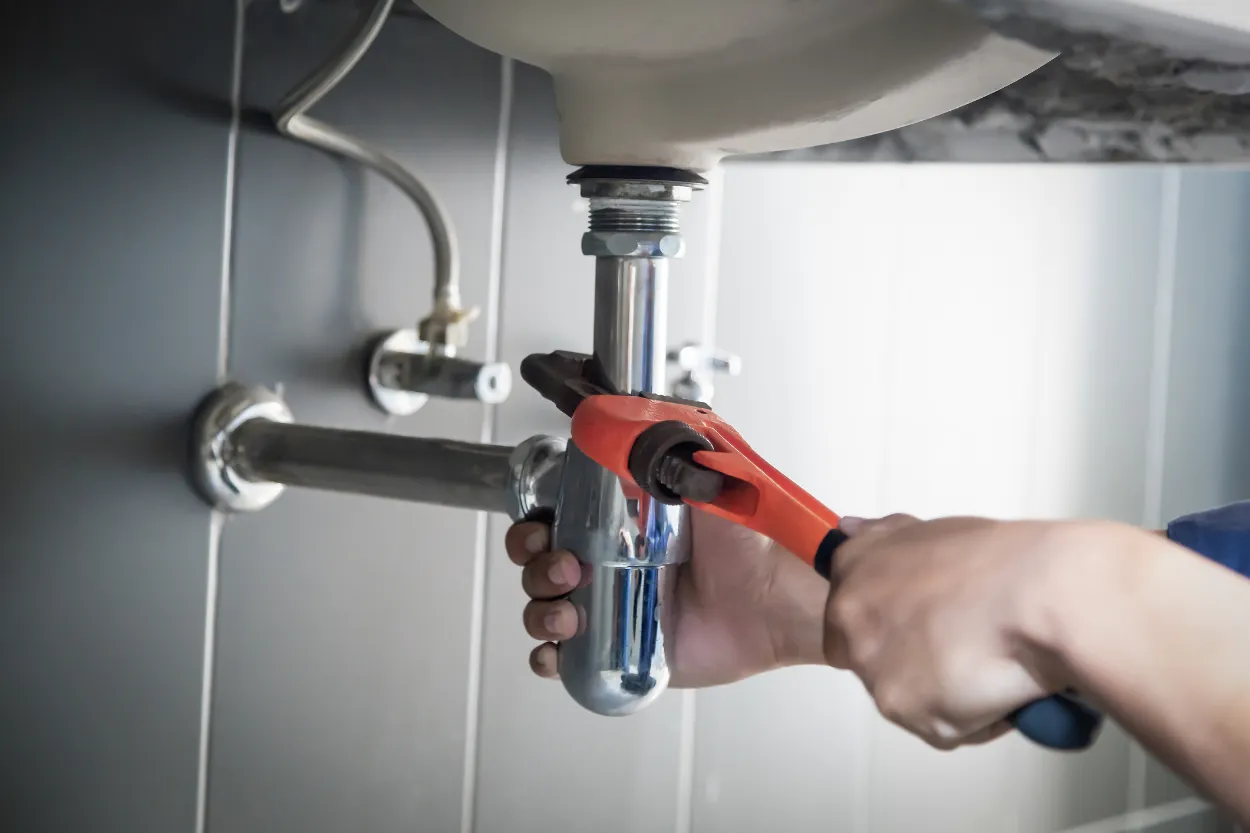 plumber using wrench on bathroom sink pipes